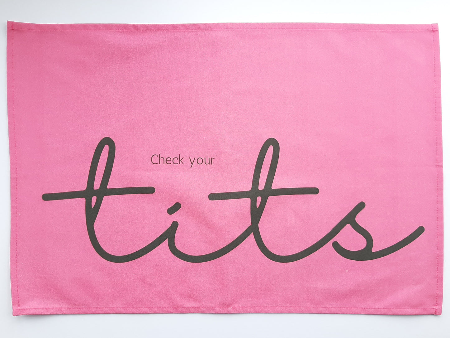 Photo of a bright pink tea towel with grey words reading Check your tits