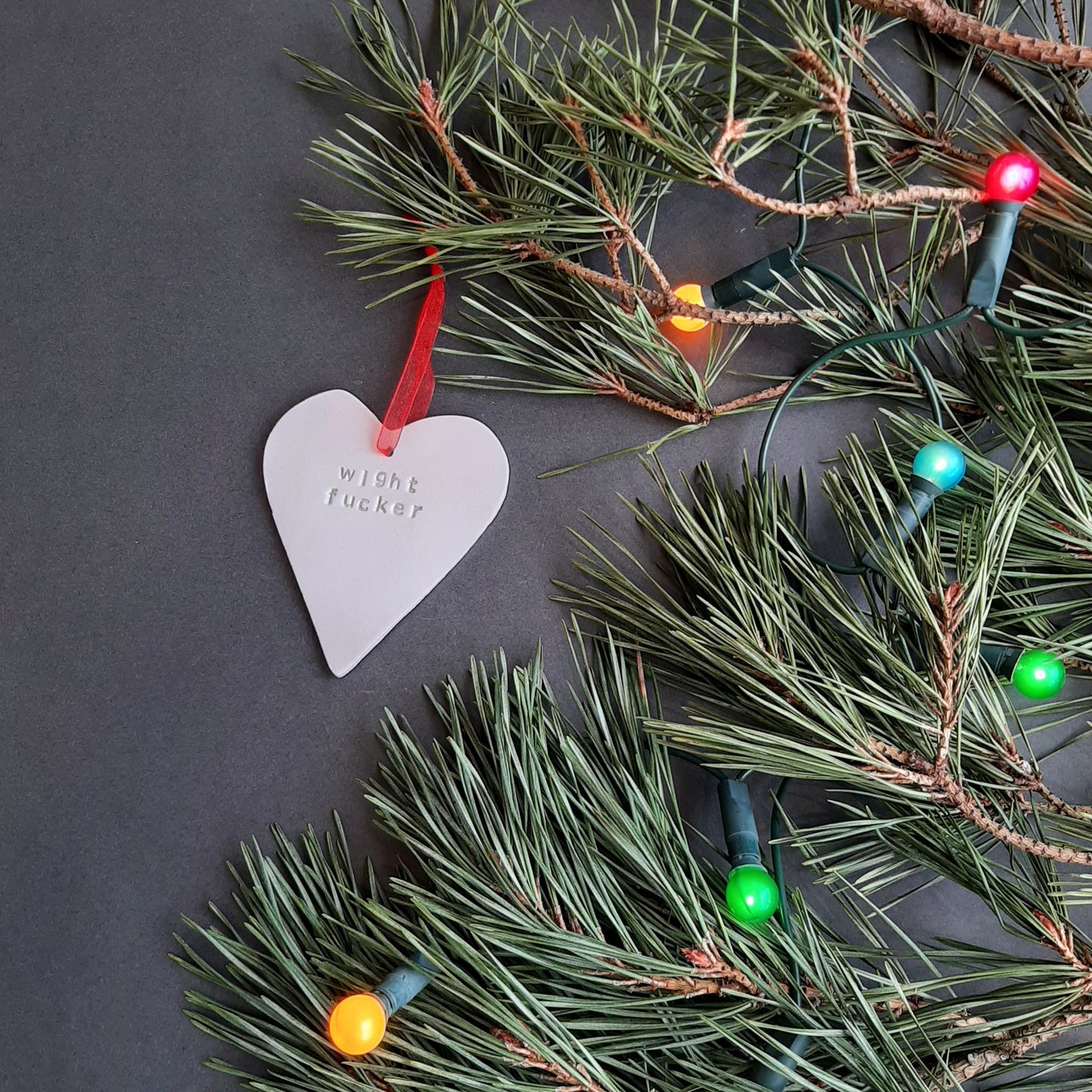 "wight fucker" hanging heart decoration  shown on foliage with coloured lights