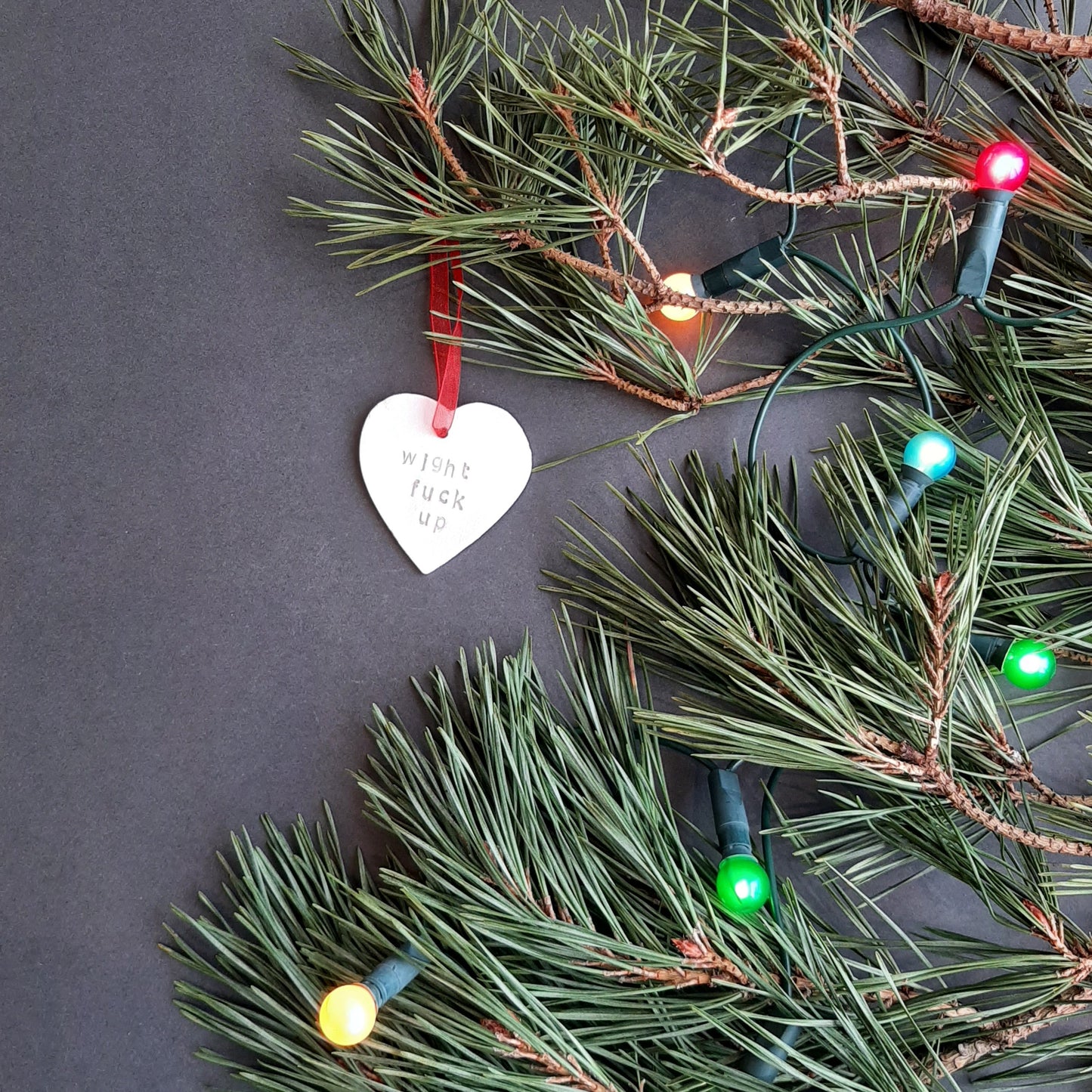 "wight fuck up" hanging heart decoration  shown on foliage with coloured lights